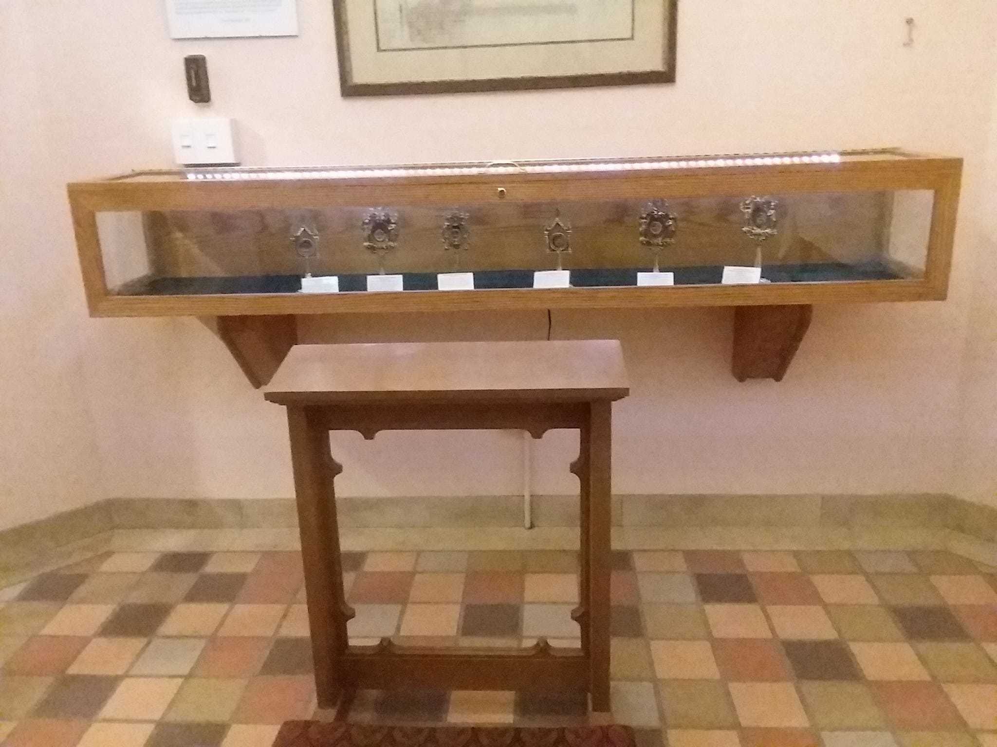 A kneeler in front f a display case full of SIX different saints' bones in their odd, award trophy like cases.